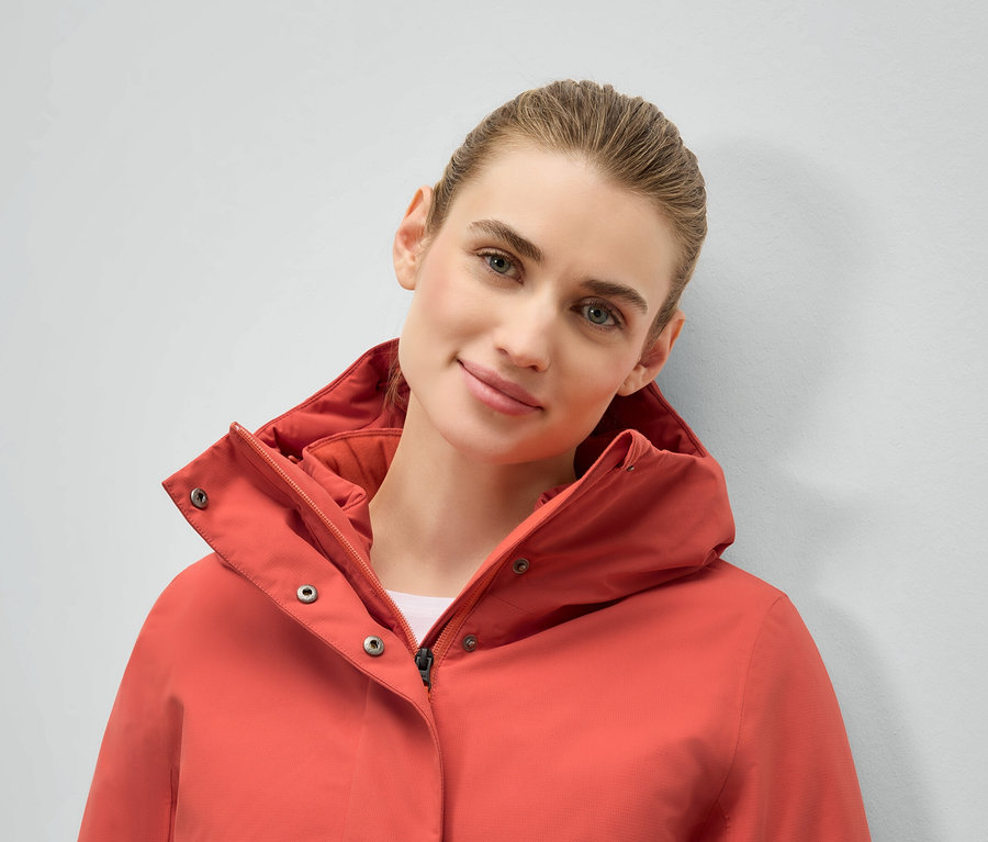 Portrét ženy v korálové bundě s kapucí.