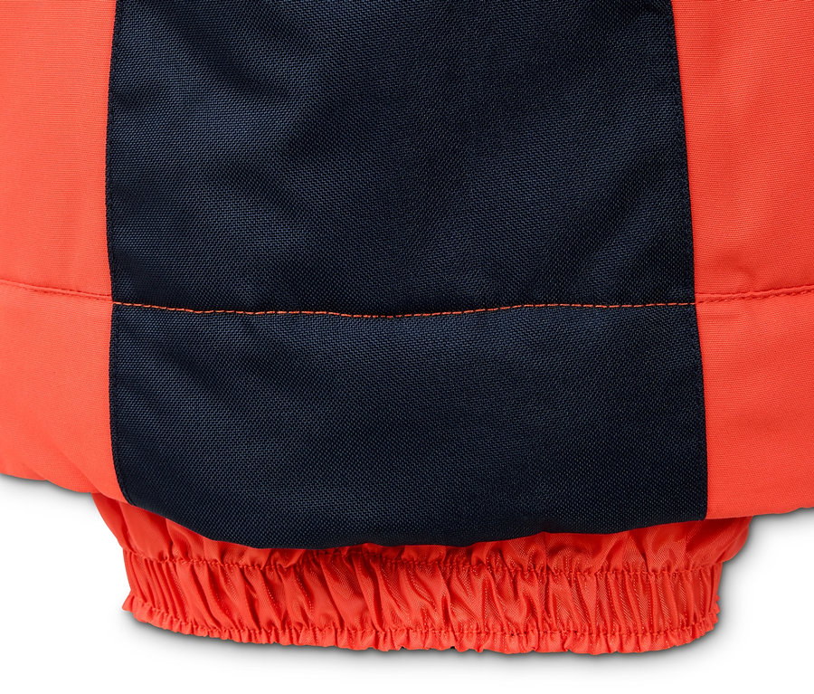 Detail oranžových snowboardových kalhot s tmavě modrým zesílením.