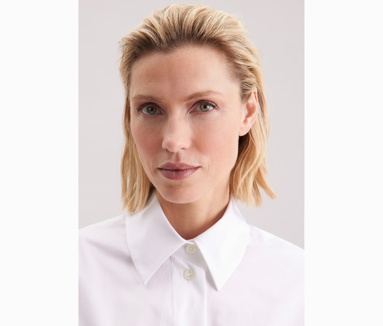 Portrét ženy s blond vlnitými vlasy v bílé halence oversize Seidensticker.