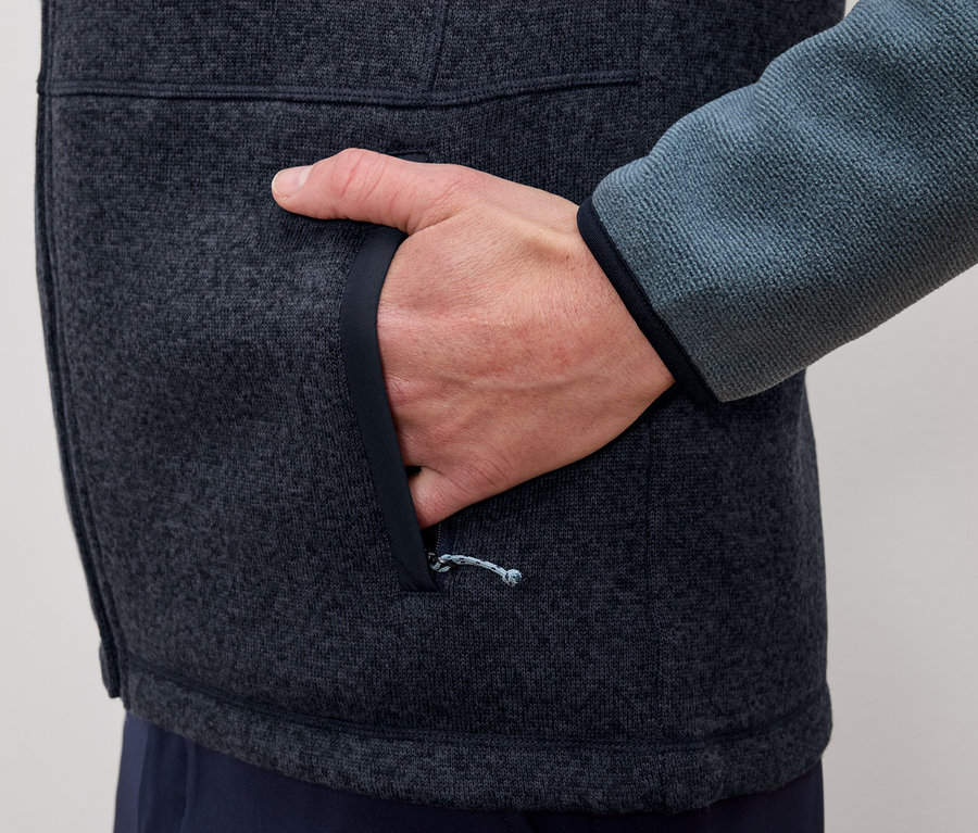 Muž dává ruku do kapsy šedo-modré fleecové bundy.