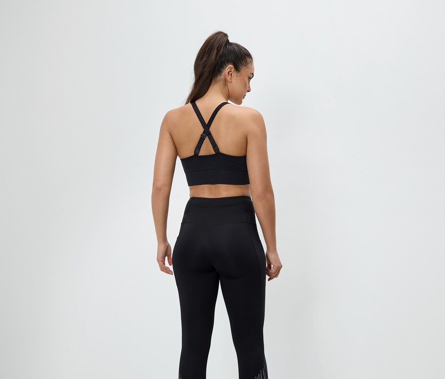 Zezadu je vidět žena v černém sportovním oblečení, má na sobě sportovní podprsenku a legíny.