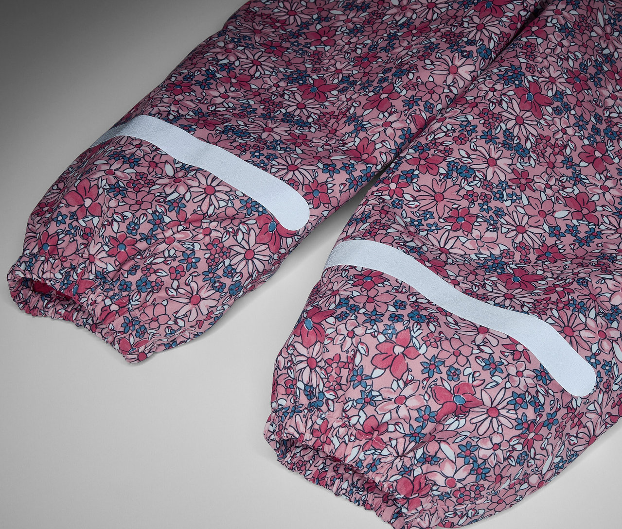 Detail dětských termo kalhot do deště s květinovým vzorem a reflexními pruhy.