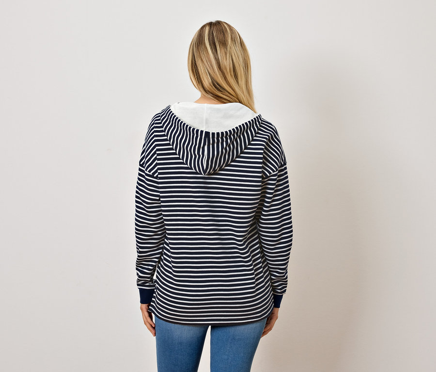 Zezadu je vidět žena s blond vlasy, která má na sobě modrobílou pruhovanou mikinu s kapucí a džíny.