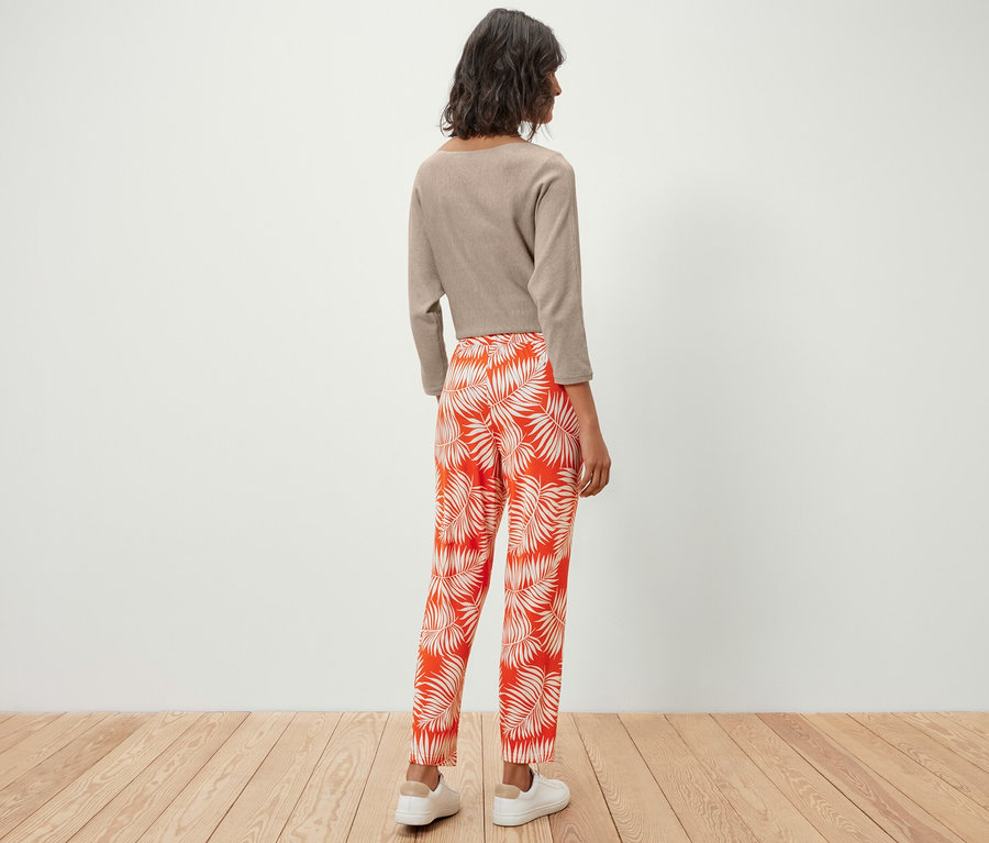 Žena stojí zády a má na sobě žerzejové kalhoty s potiskem a top.