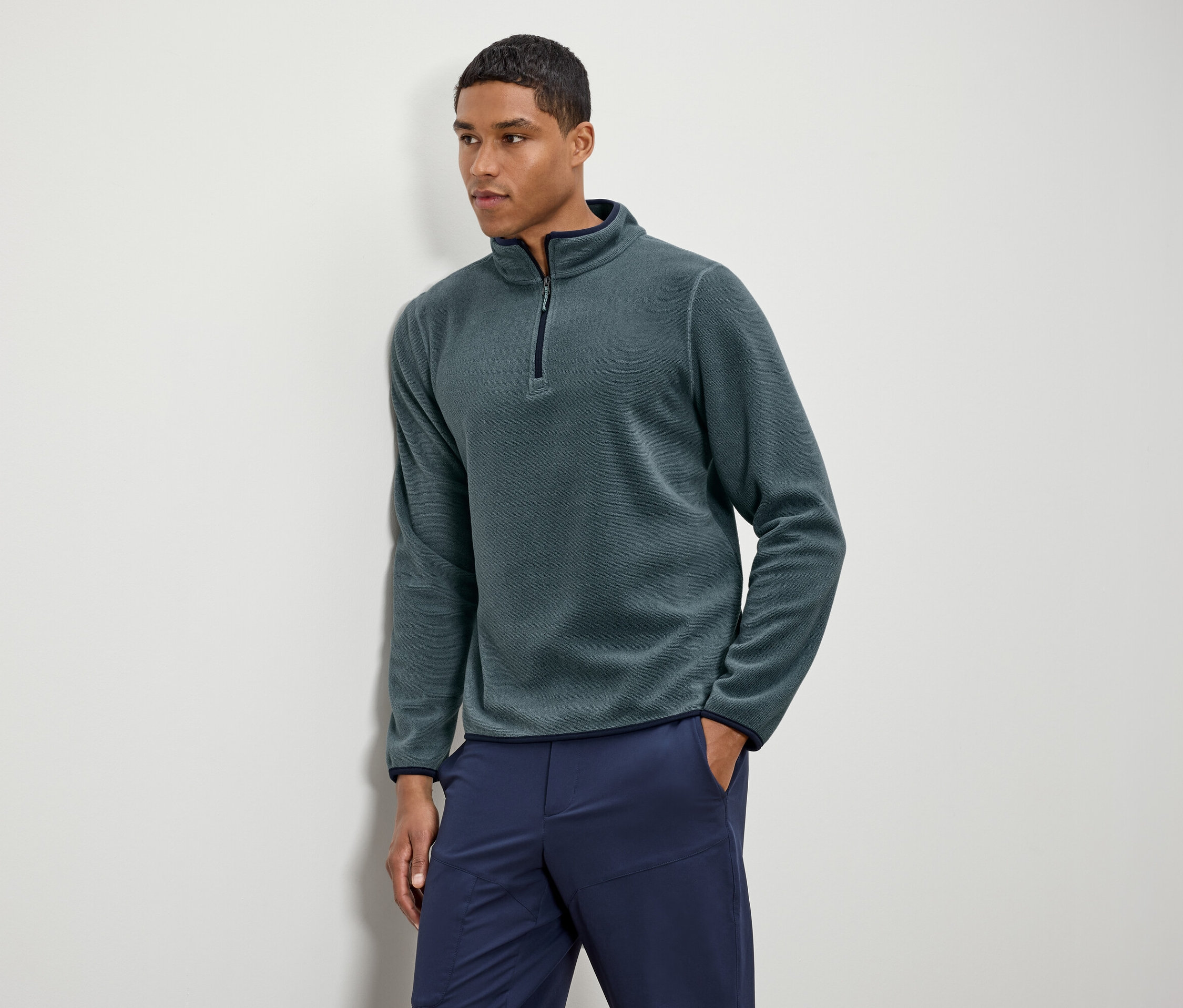 Muž má na sobě zelenou fleecovou mikinu s tmavě modrými kalhotami.