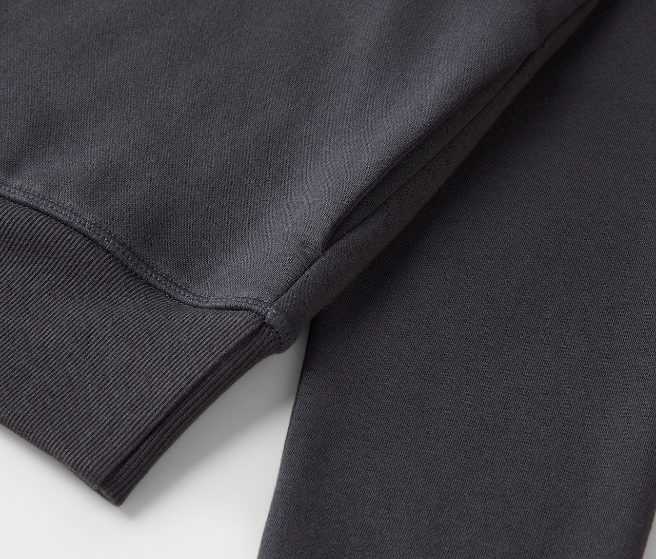 Detail šedé mikiny s žebrovaným lemem na rukávu.