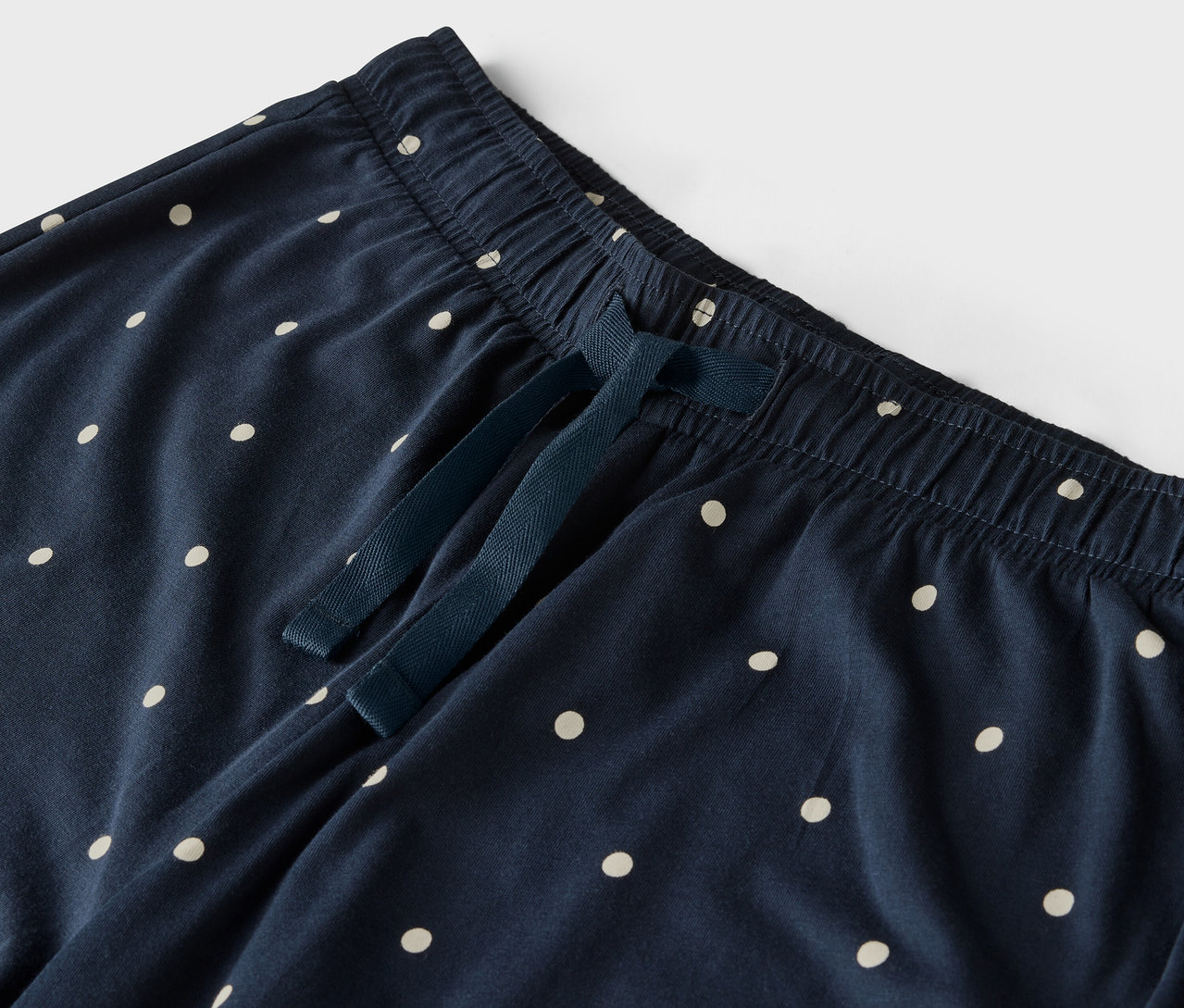 Detail modrých kalhot s bílými puntíky, elastickým pasem a stahovací šňůrkou.