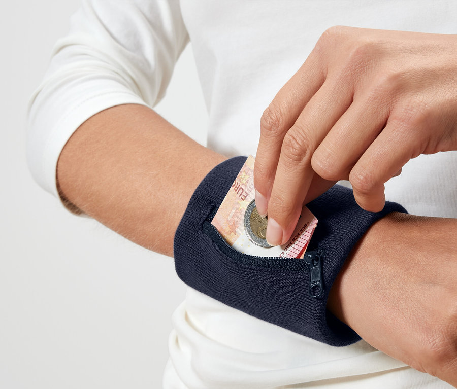 Osoba vkládá eurovou minci do tmavě modrého náramkového pouzdra.