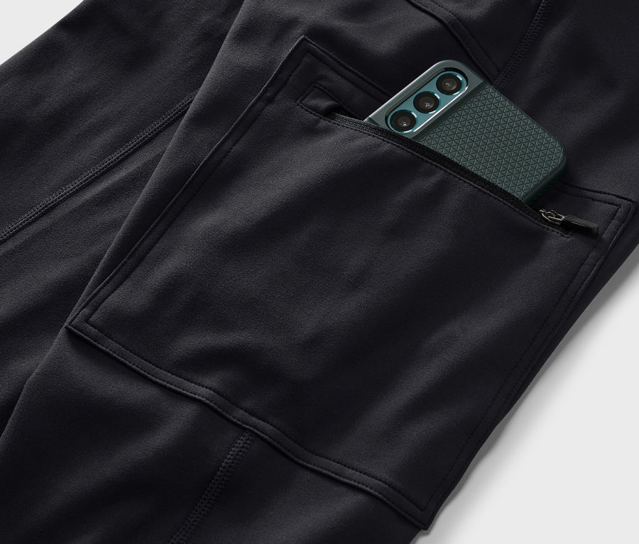 Detail černých outdoorových legín s kapsou, ve které je zelený mobilní telefon.