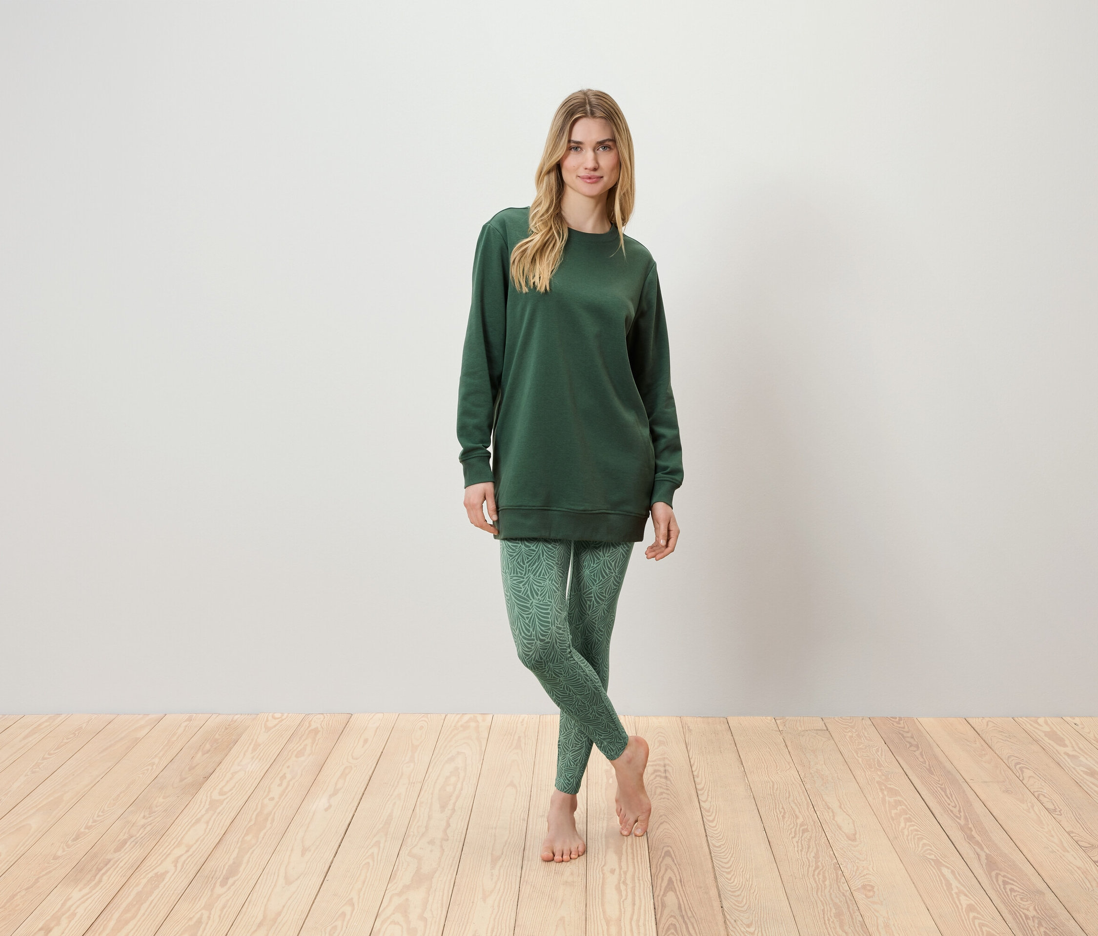 Žena stojí a má na sobě zelenou tuniku a zelené legíny.