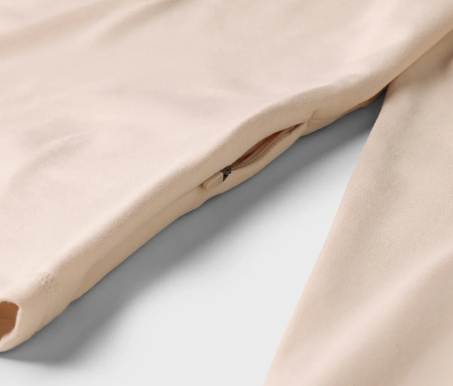 Detail béžového oděvu s kapsou na zip na boku.