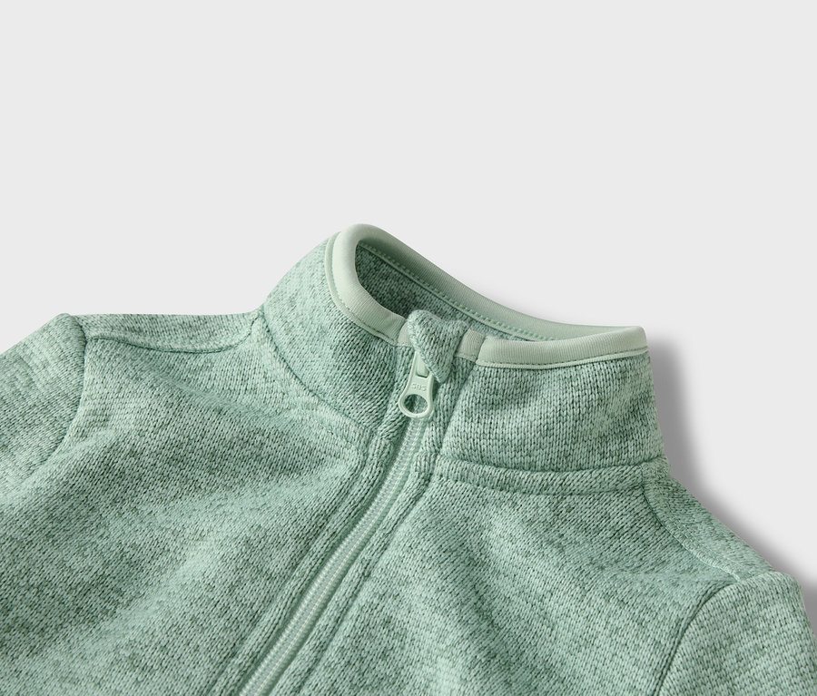 Detailní záběr na světle zelenou fleecovou bundu na zip.