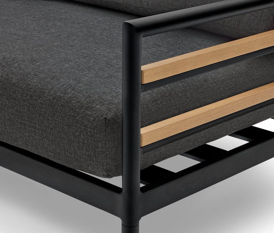 Detailní záběr na křeslo s šedým polštářem, černým rámem a dřevěnými detaily.