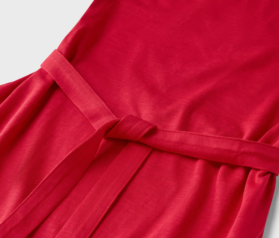 Detail červených šatů se zavázaným páskem.