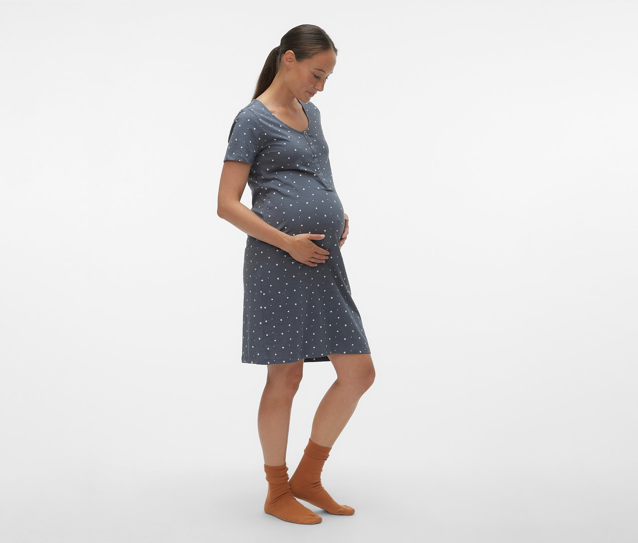 Těhotná žena z profilu má na sobě modrou noční košili MAMALICIOUS »MLMIRA« s bílými puntíky a hnědé ponožky.