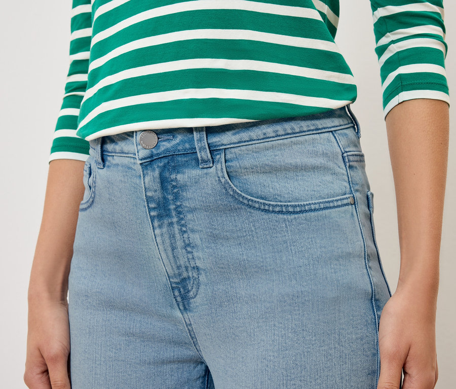 Detail osoby v světle modrých džínách a zeleno-bíle pruhovaném topu.