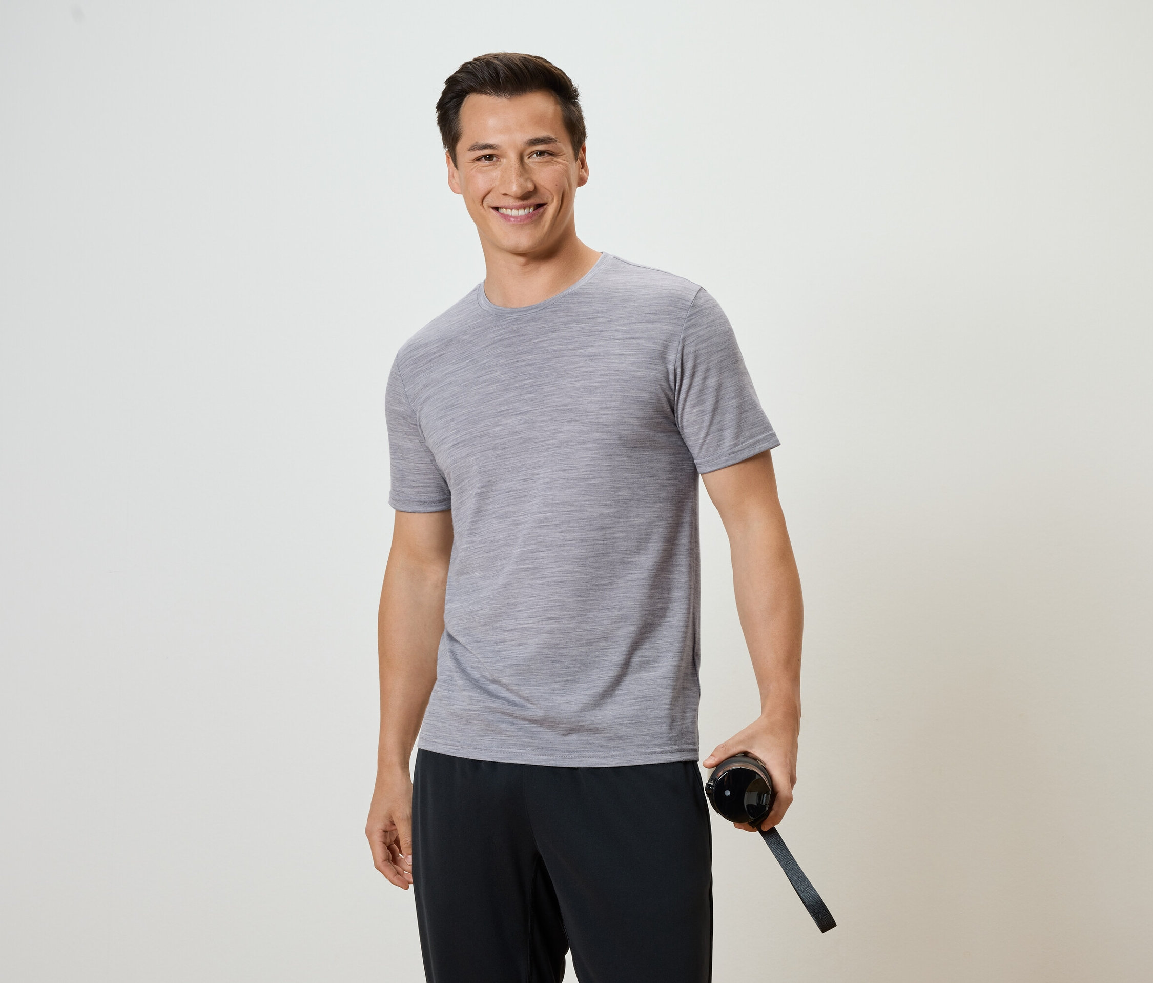 Muž v šedém tričku a černých kalhotách drží láhev s vodou.