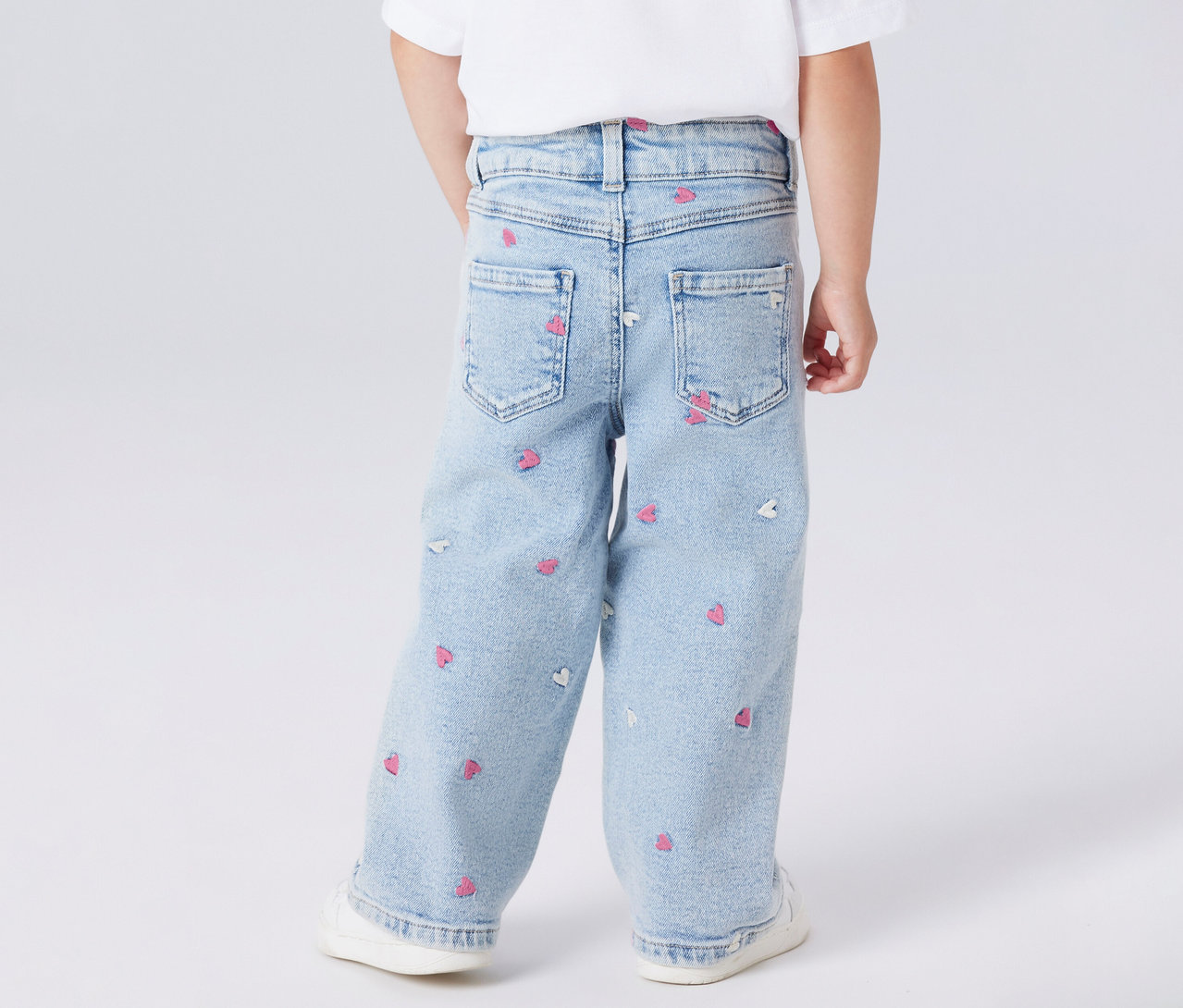 Dítě zezadu v dětských džínách Wide Leg NAME IT se vzorem srdce a bílých botách.