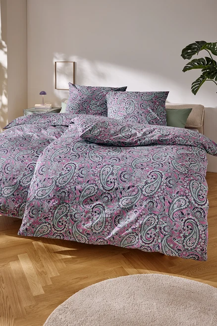 Detailní záběr na postel s růžovým ložním prádlem s paisley vzorem.