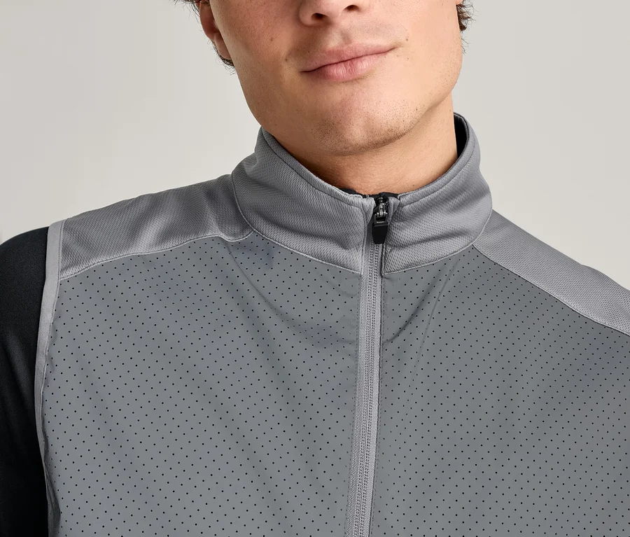 Detail muže v šedé vestě na zip přes černé tričko s dlouhým rukávem.