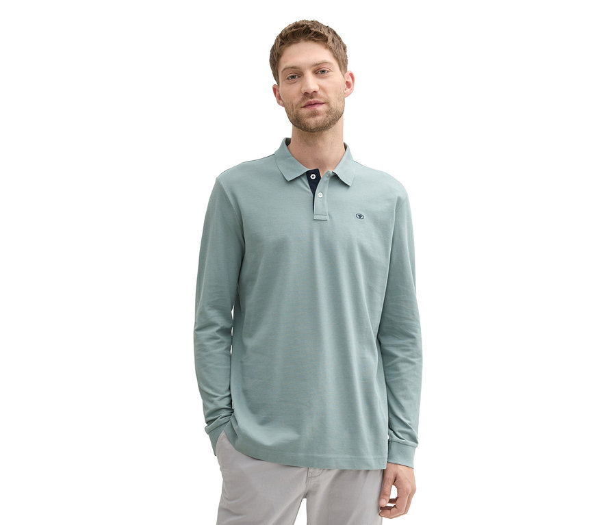 Muž v mátově šedé polokošili z piké s dlouhým rukávem Tom Tailor a šedých kalhotách stojí na bílém pozadí.