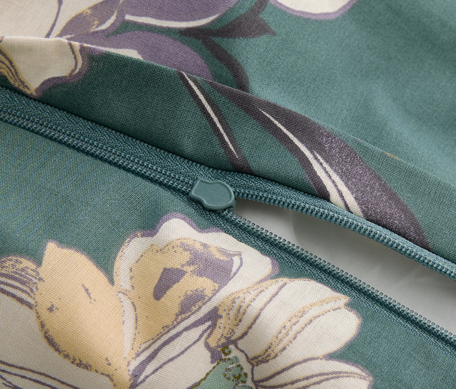Detailní záběr na zip na nazelenalé látce s květinovým vzorem.