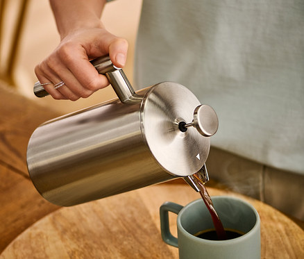 Žena nalévá kávu z dvoustěnné konvice french press z ušlechtilé oceli o objemu 900 ml do hrnku.