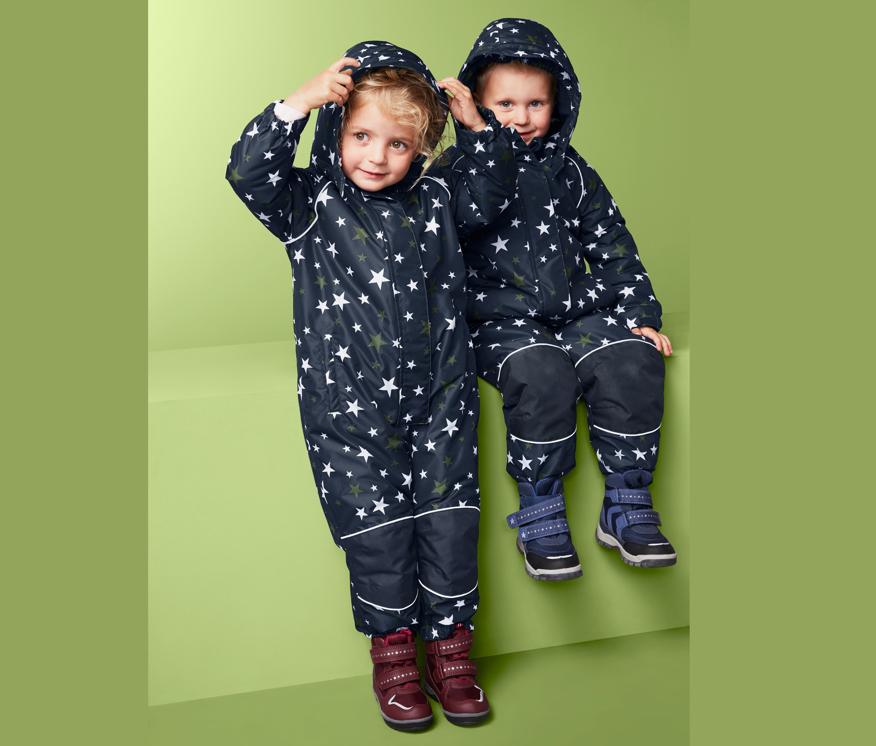 Děti v zimních kombinézách s hvězdami sedí vedle sebe.