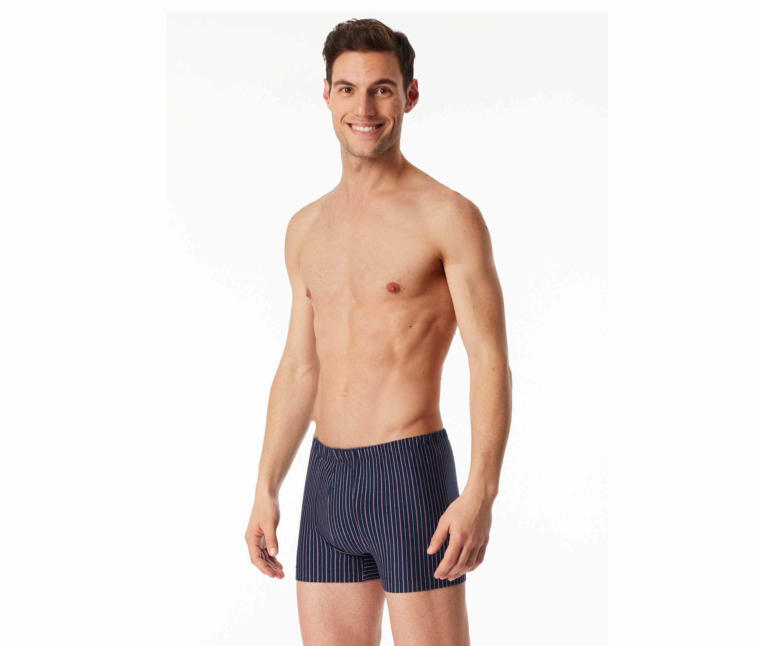 Usmívající se muž s odhalenou horní částí těla nosí pruhované boxerky na bílém pozadí.