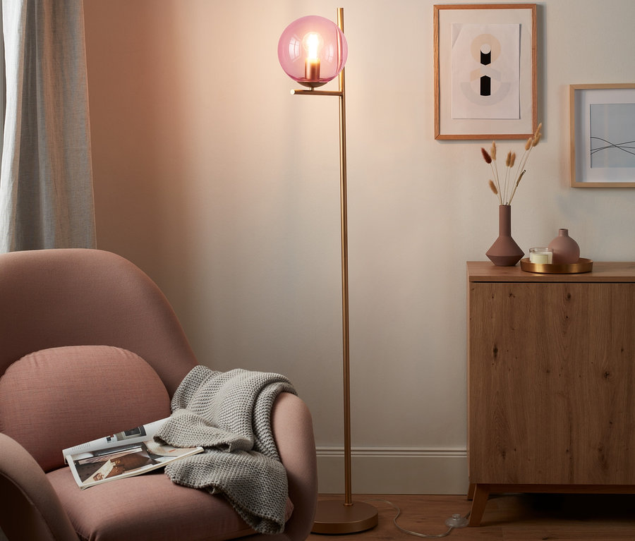 Růžové křeslo s přehozenou dekou a stojací lampa Skleněná koule v obývacím pokoji.
