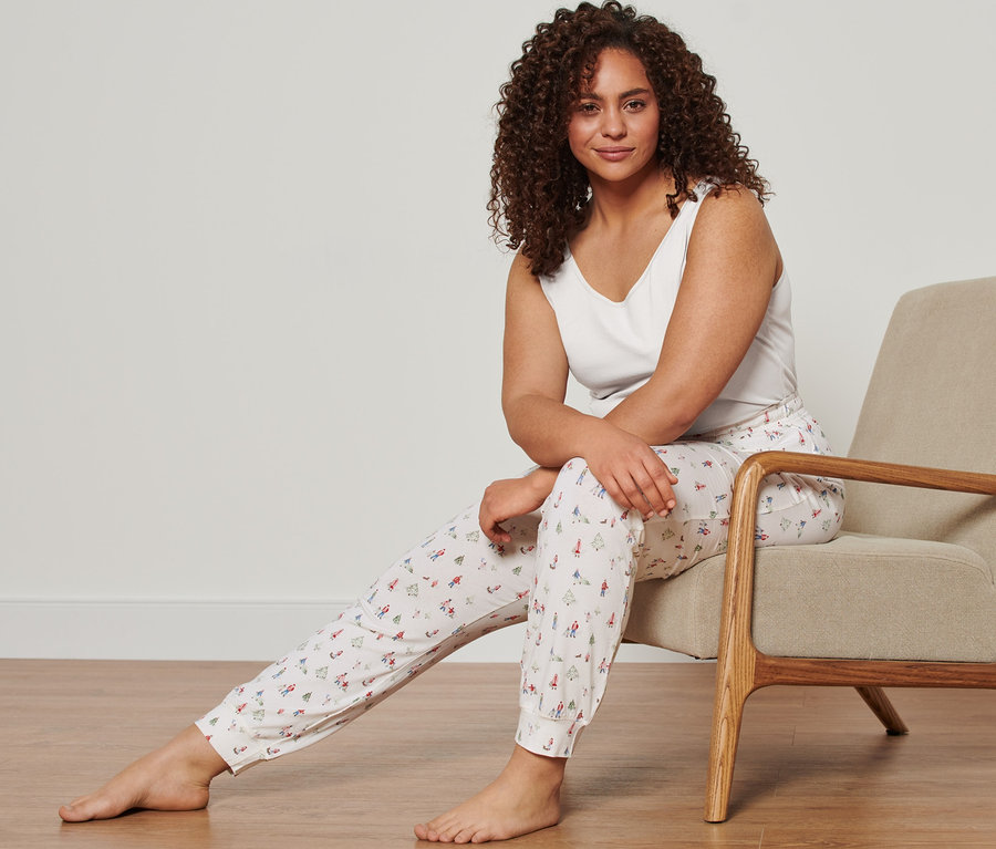 Žena sedí v křesle a má na sobě bílé tílko (Košilky, 2 ks) a žerzejové kalhoty (Pohodlné žerzejové kalhoty).