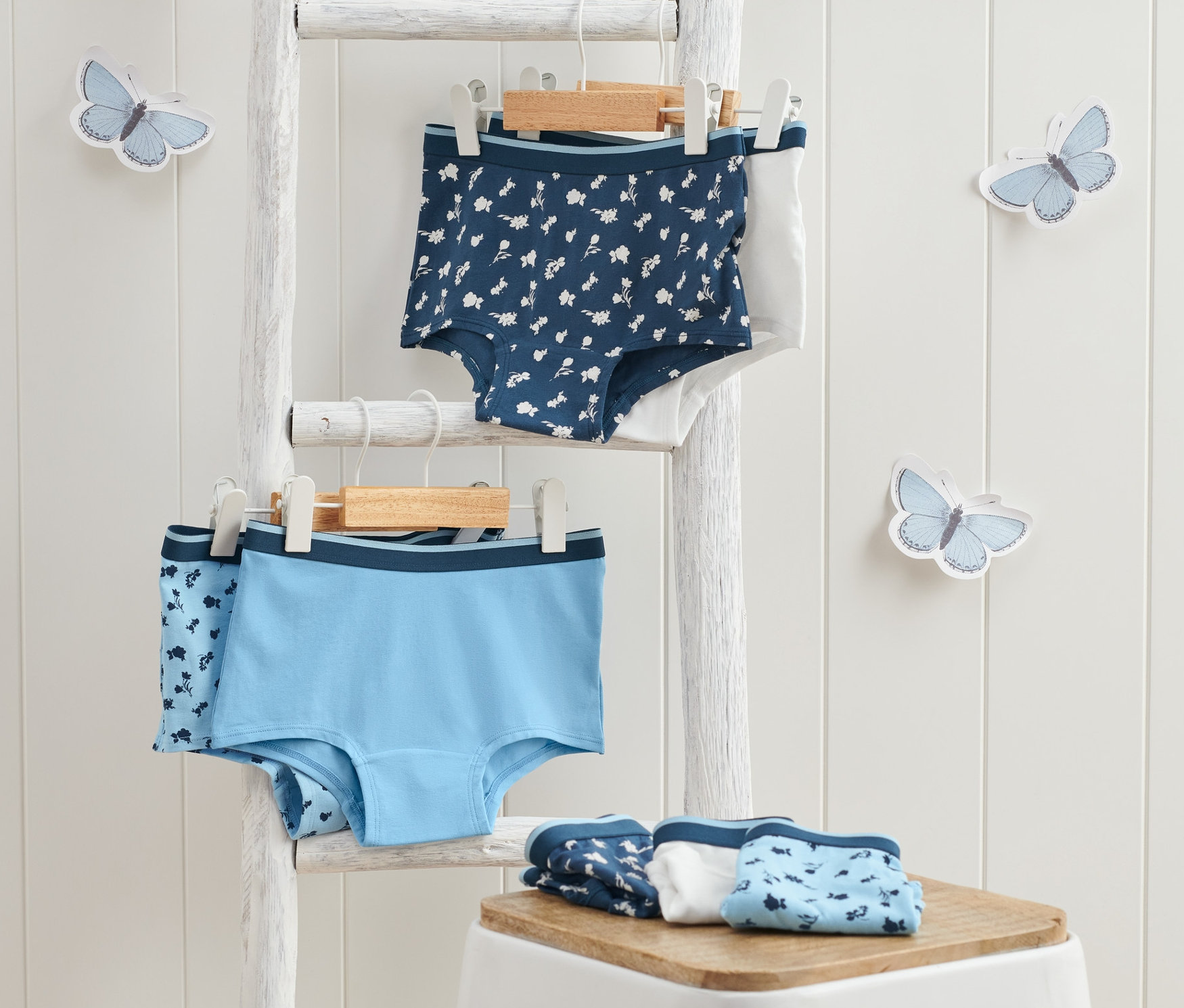 Na bílém žebříku visí dvoje dívčí kalhotky a na bílé stoličce leží složené dívčí kalhotky, 7 ks, modré.