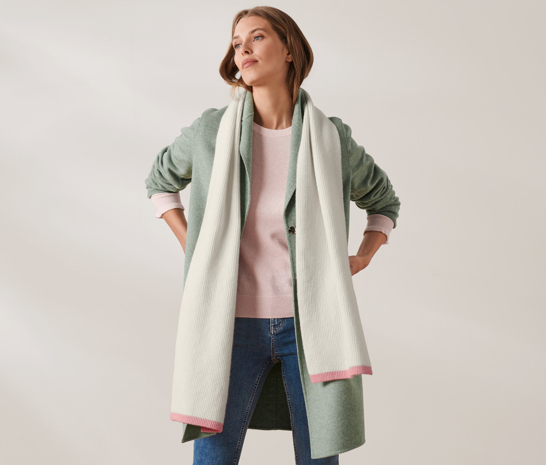 Žena pózuje s rukama v bok a má na sobě pletenou šálu s vlnou.