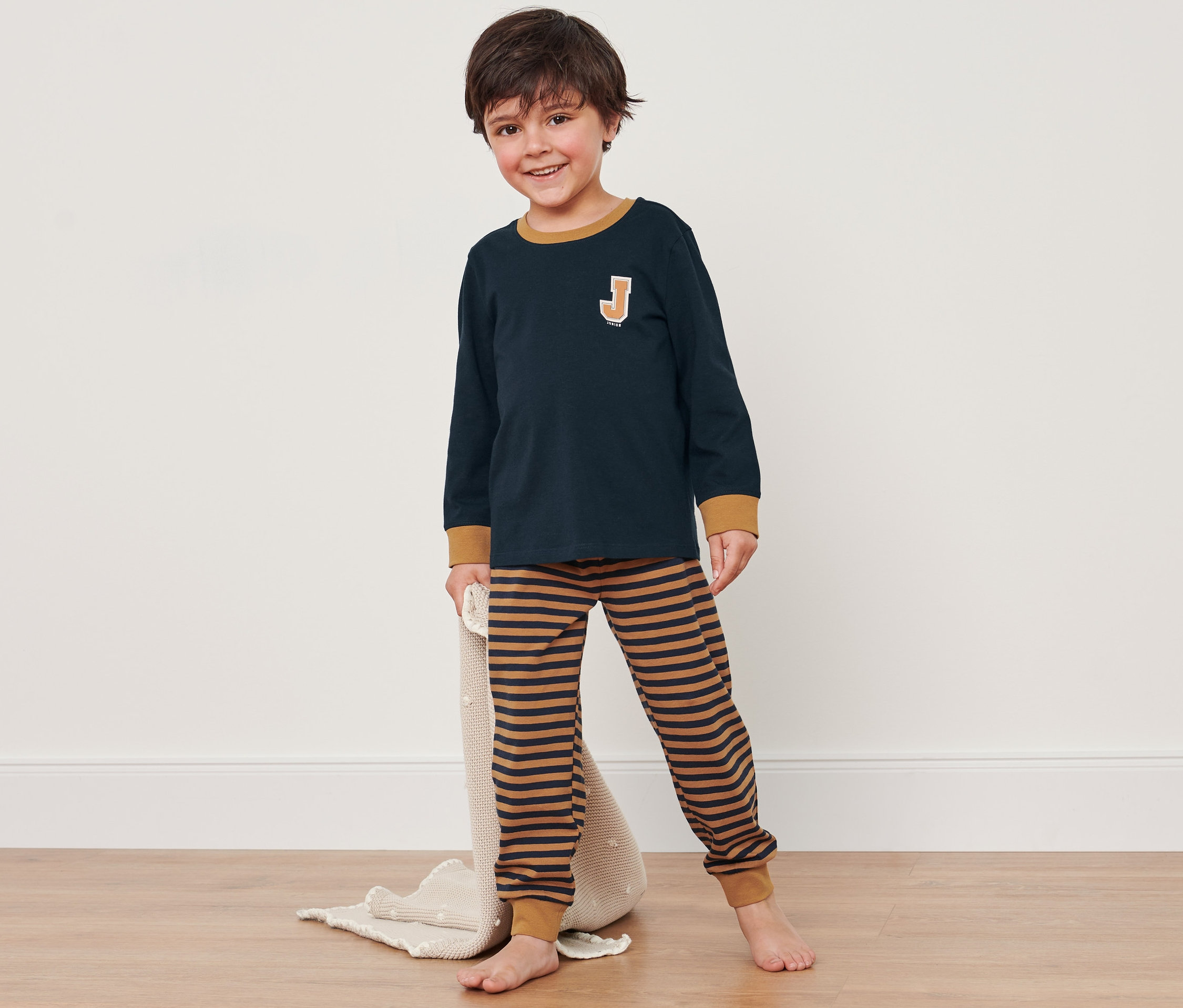 Chlapec v modro-hnědém pyžamu stojí na podlaze a drží deku.