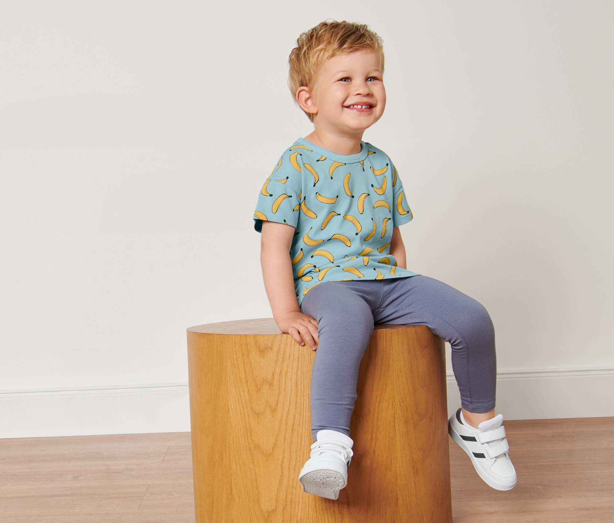 Chlapec sedí na dřevěné stoličce a má na sobě světle modré tričko s potiskem banánů.