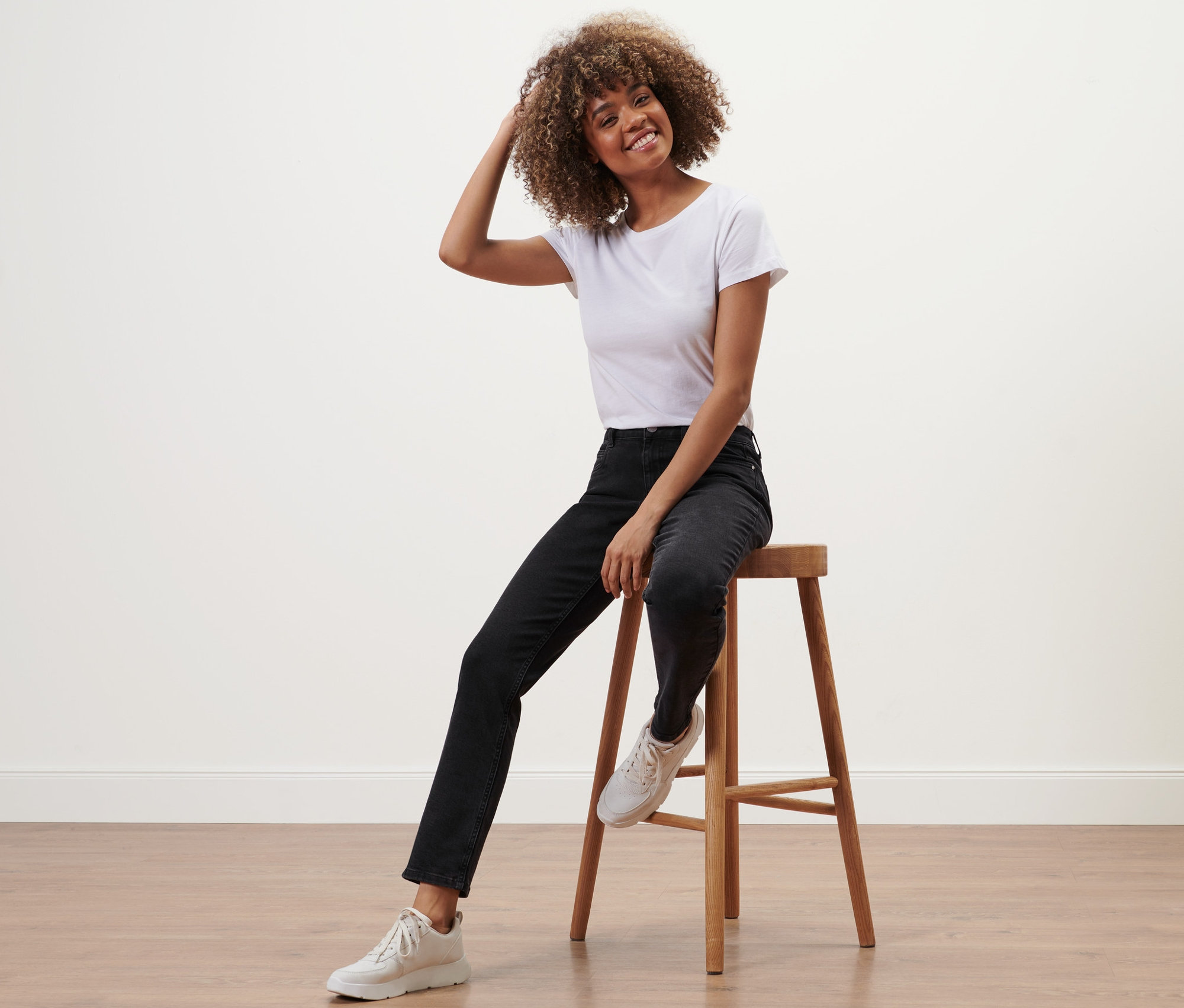 Žena sedí na stoličce a má na sobě černé rovné džíny »Fit Juna«.