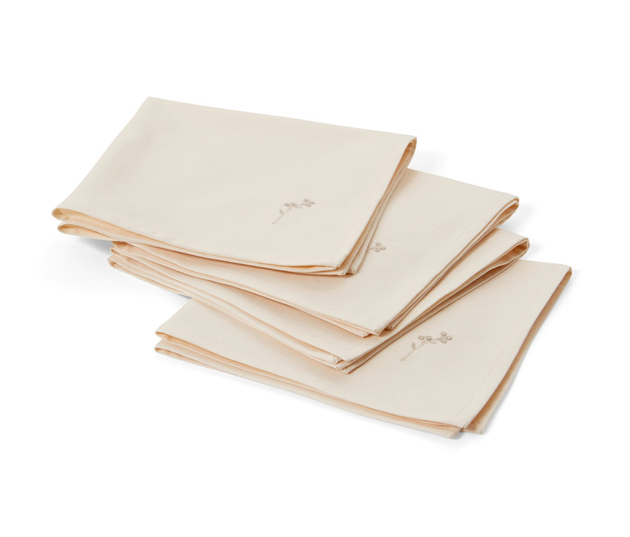 Čtyři krémové ubrousky s výšivkou leží složené na sobě.