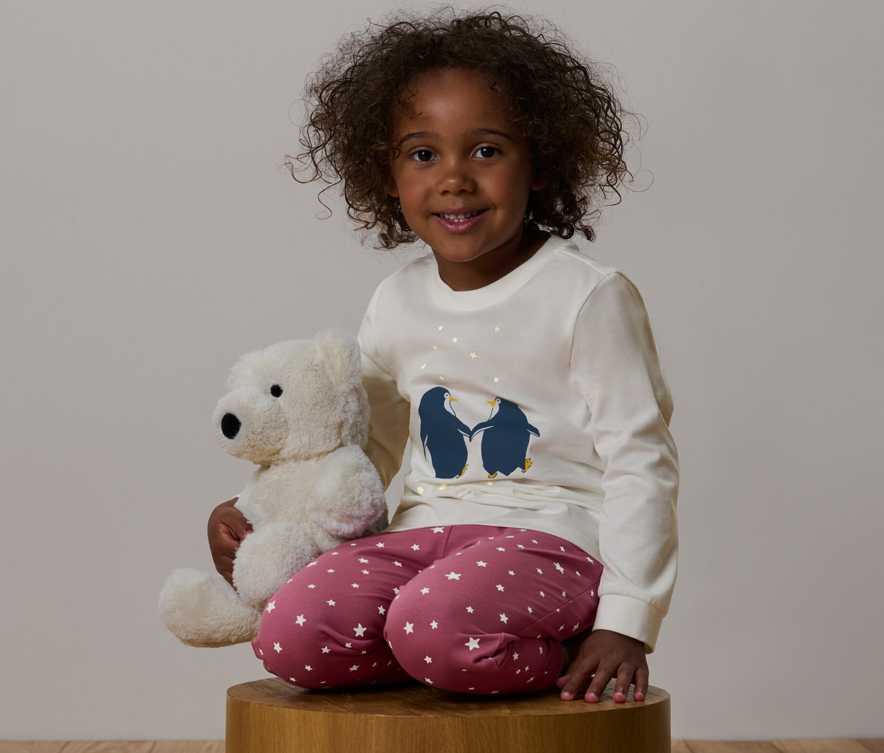 Dívka sedí a objímá plyšového medvídka, má na sobě růžové dětské pyžamo »Glow in the dark«.