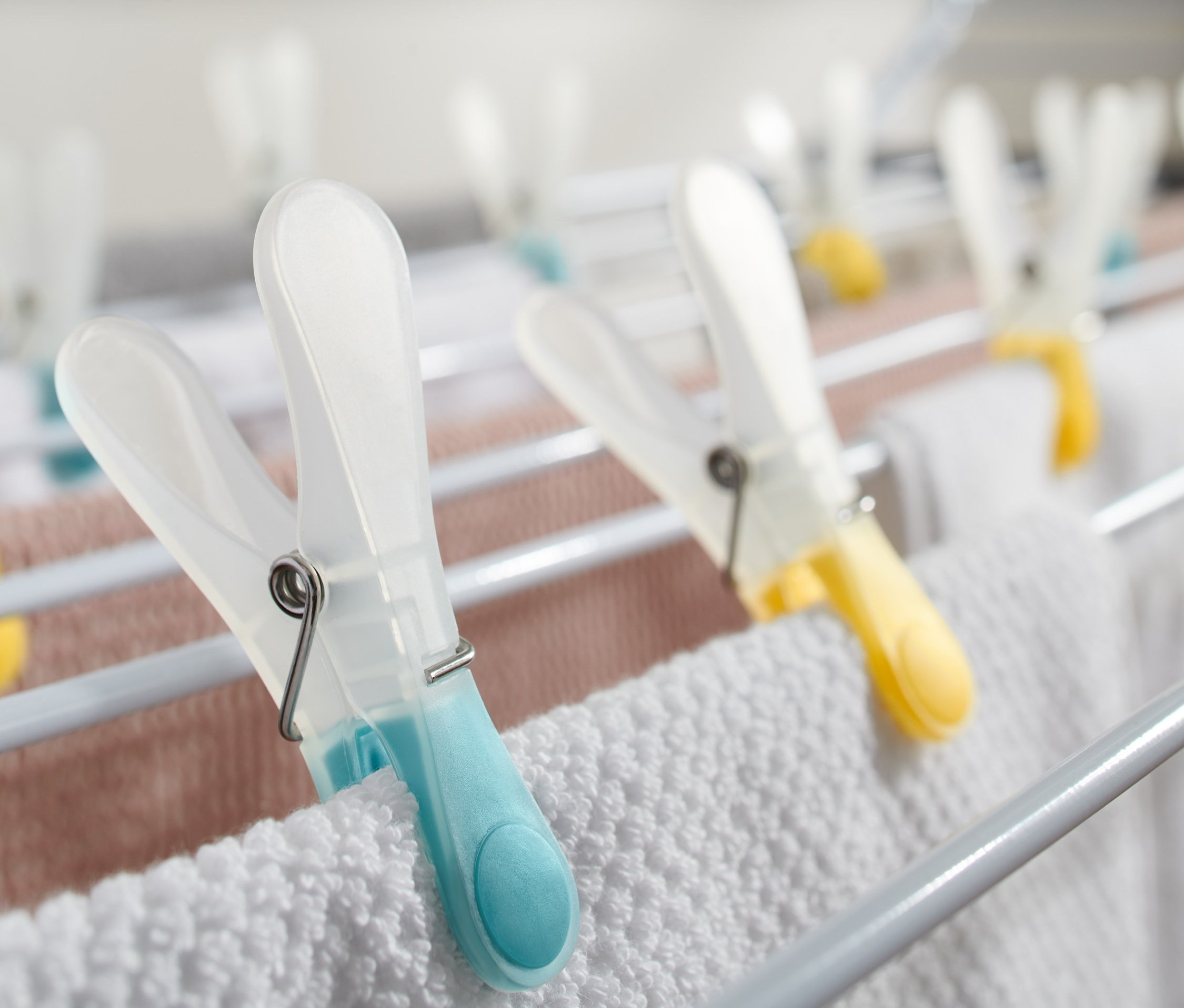 Detail bílého sušáku na prádlo s barevnými kolíčky na prádlo, 20 ks, držícími bílé a růžové prádlo.