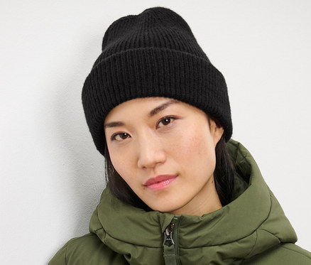 Žena má na sobě černou pletenou čepici a zelenou bundu.