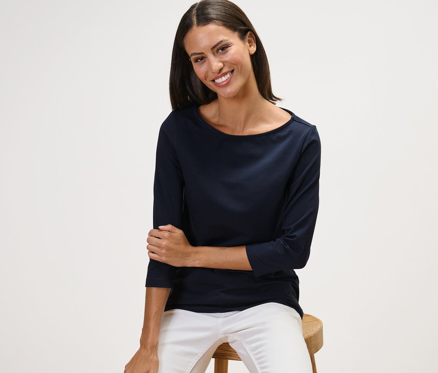 Žena sedí na stoličce a má na sobě námořnicky modré triko s 3/4 rukávem.