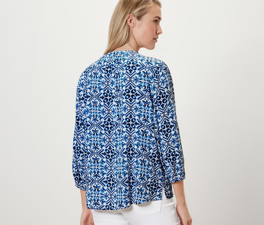 Žena má na sobě modrou tunikovou halenku s potiskem.