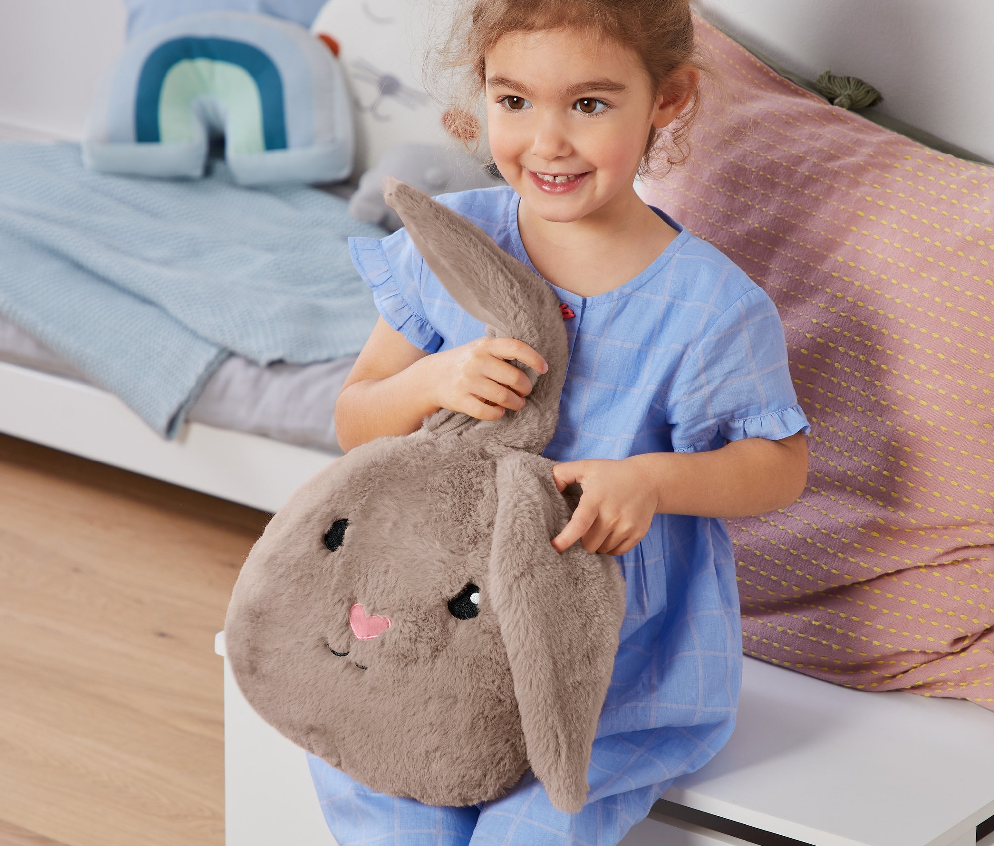 Usmívající se holčička v modrém pyžamu drží plyšového zajíce.