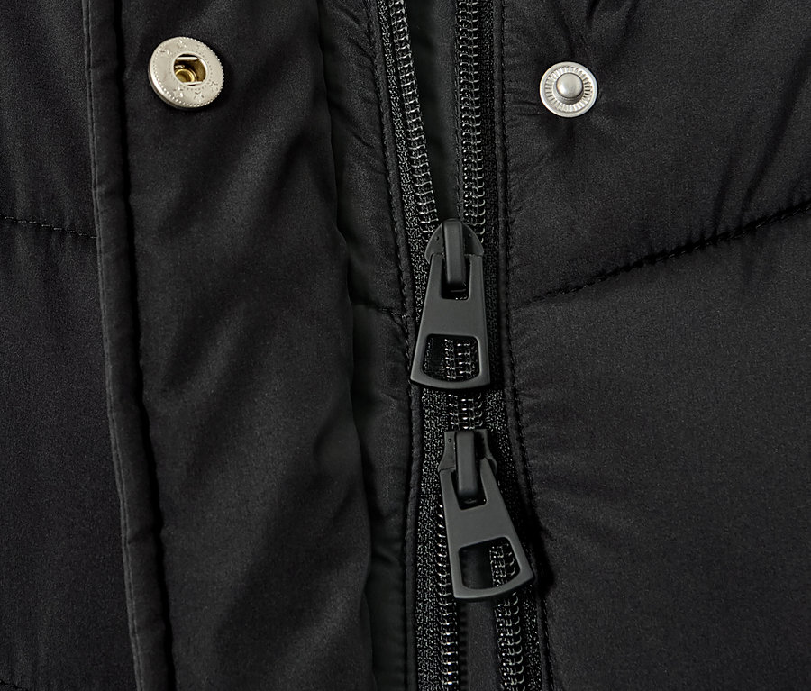 Detail černého prošívaného kabátu s kapucí, ukazující zip a patentky.