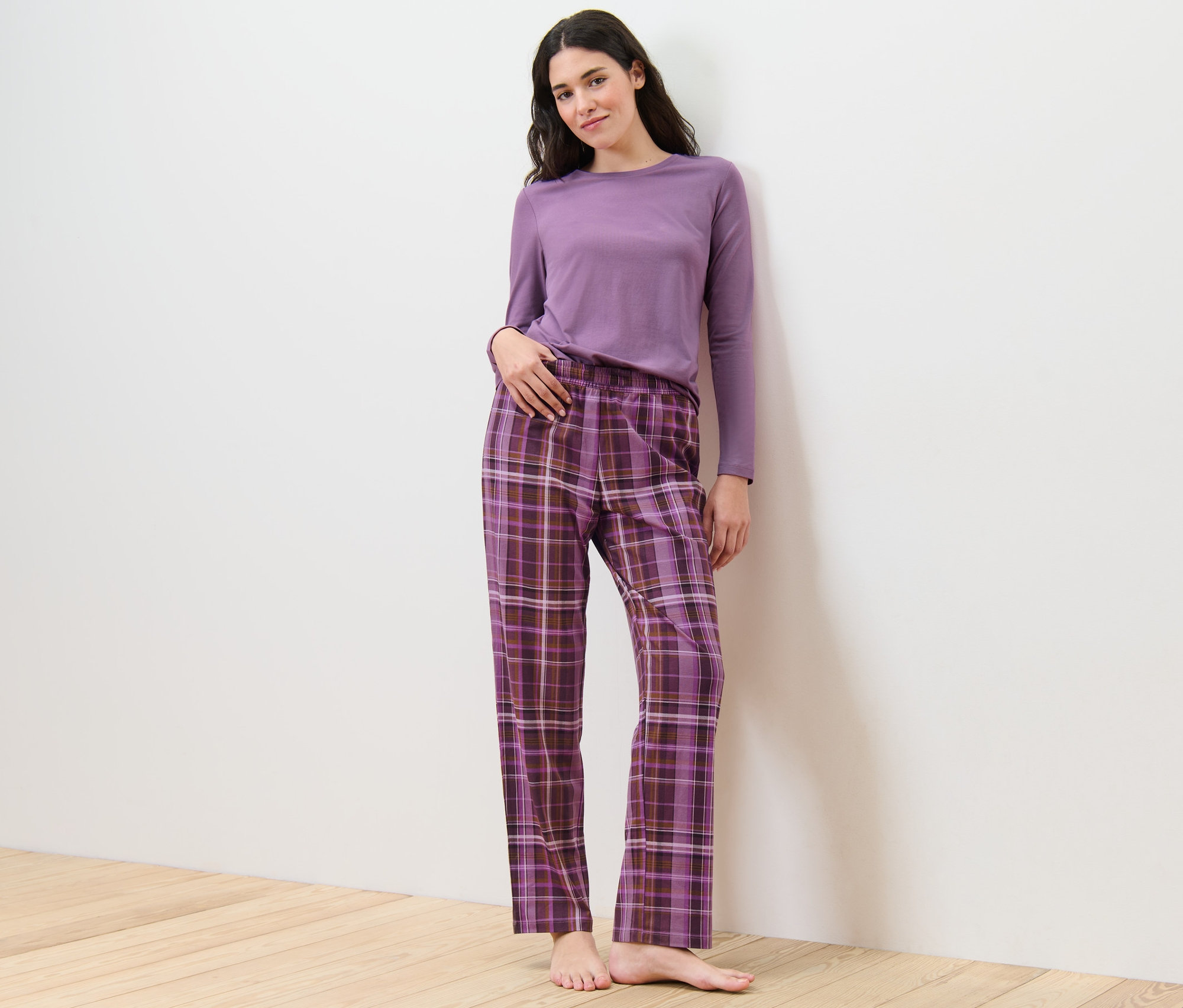 Žena pózuje v pyžamu s kostkovanými kalhotami.