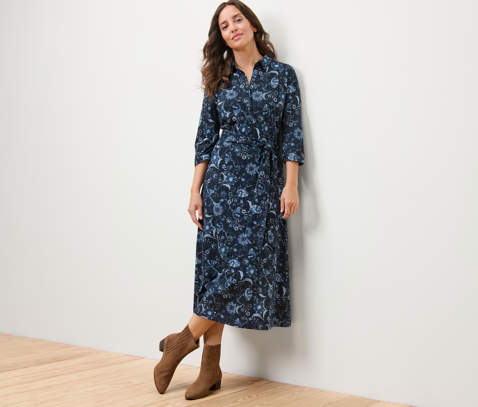 Žena pózuje v džerzejových šatech s potiskem a hnědých kozačkách.