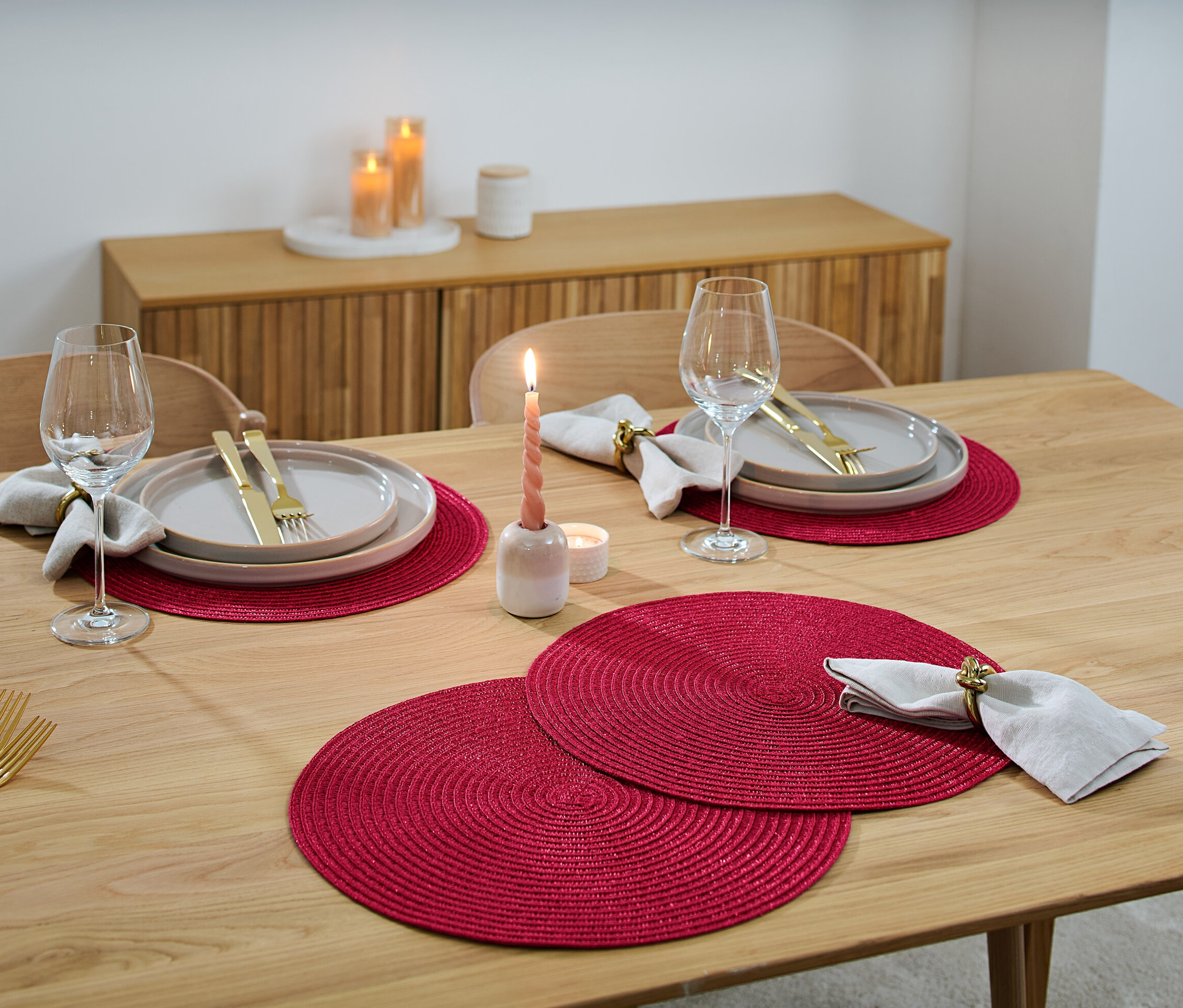 Na dřevěném stole jsou prostírání, talíře, sklenice na víno, příbory a svíčky.