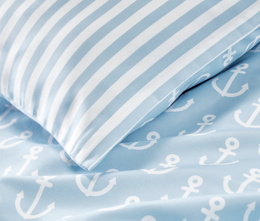 Detail modrého povlečení z mikrovlákna s potiskem bílých kotev a pruhovaného polštáře.