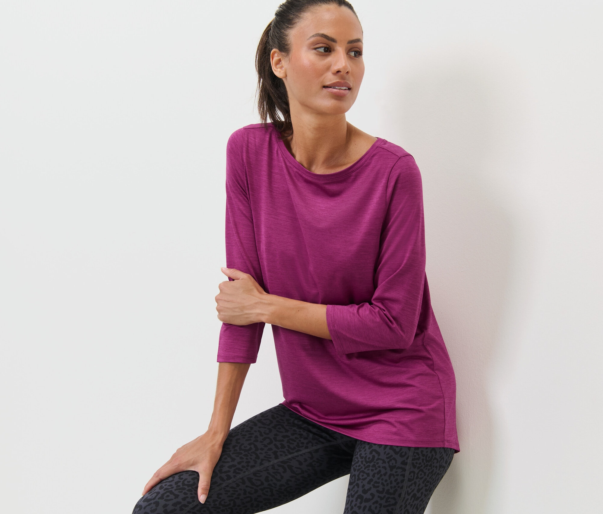 Žena opírající se o zeď má na sobě růžové funkční triko s tříčtvrtečními rukávy a legíny se zvířecím potiskem.