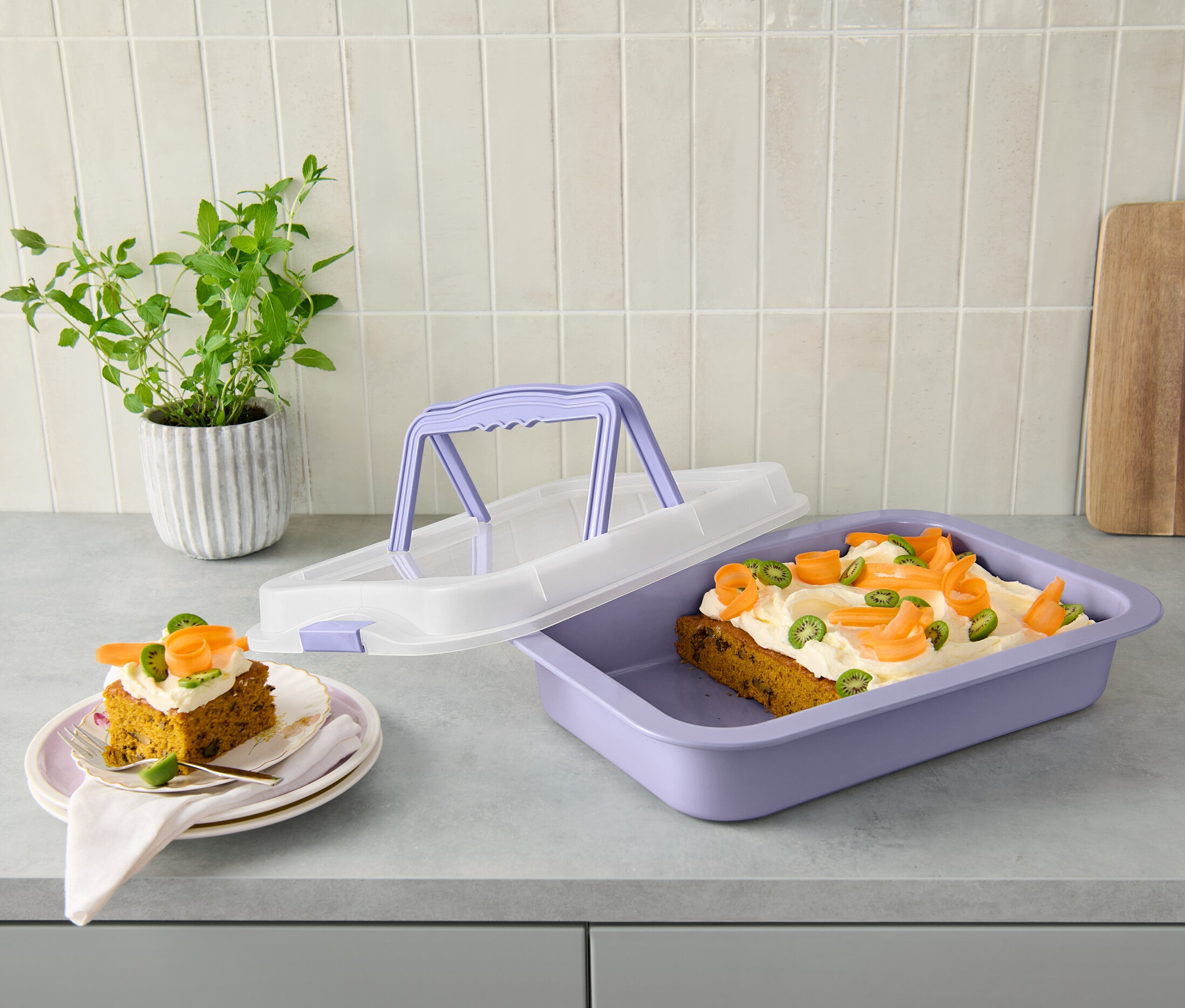 Dva kousky dortu na talířích a pekáč s víkem s dortem na lince.